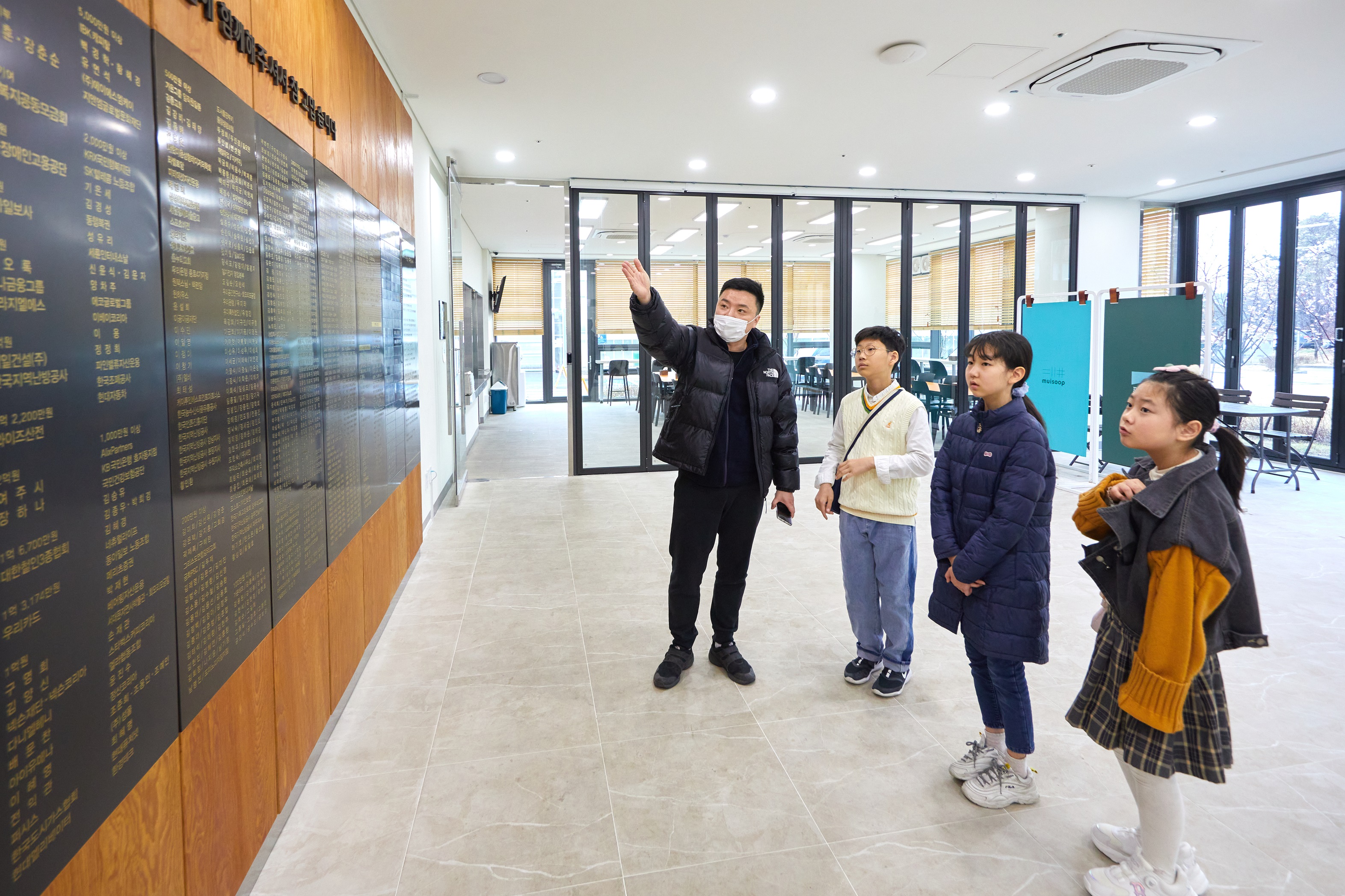 김상우(왼쪽) 푸르메소셜팜 기획팀장에게 푸르메소셜팜 건립 과정에 대한 설명을 듣고 도움을 준 분들의 이름이 적힌 기부벽을 살펴보는 소중 학생기자단.